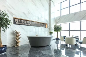 A modern interior with a marble reception desk, a large bathtub, and a seating area with chairs and tables.