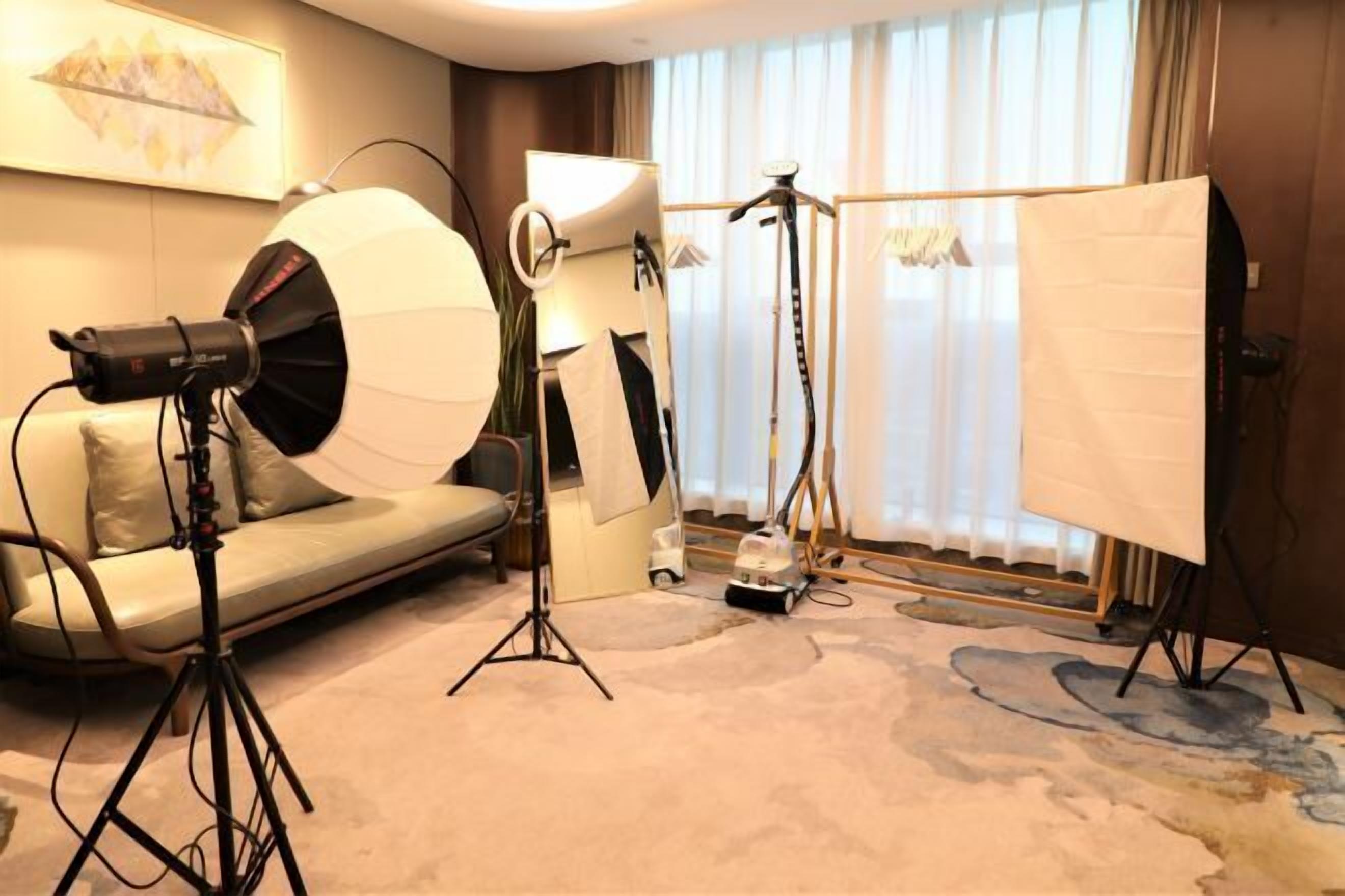 A room with a sofa, a tripod, a ring light, and a backdrop stand.