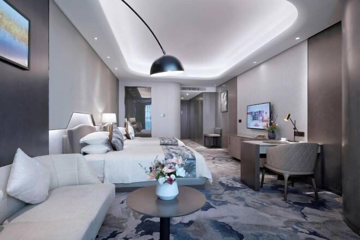 Een moderne hotelkamer met een bed, een bureau, een stoel, een bank en een kleine tafel met een bloevas.