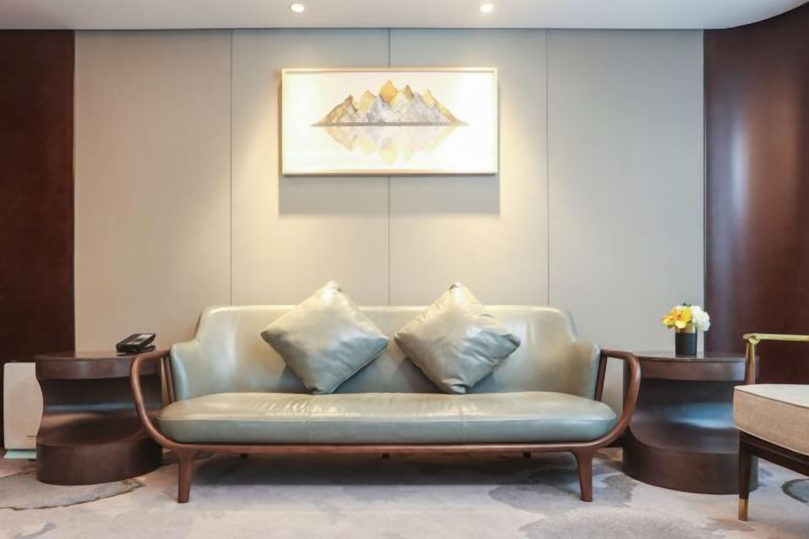 A modern room with a light-colored leather sofa, two matching cushions, a framed artwork above the sofa, and a small table with a vase of flowers.