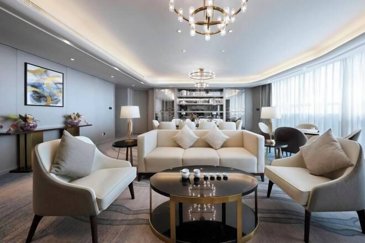 Een moderne hotellobby met een ronde salontafel, banken en een kroonluchter.