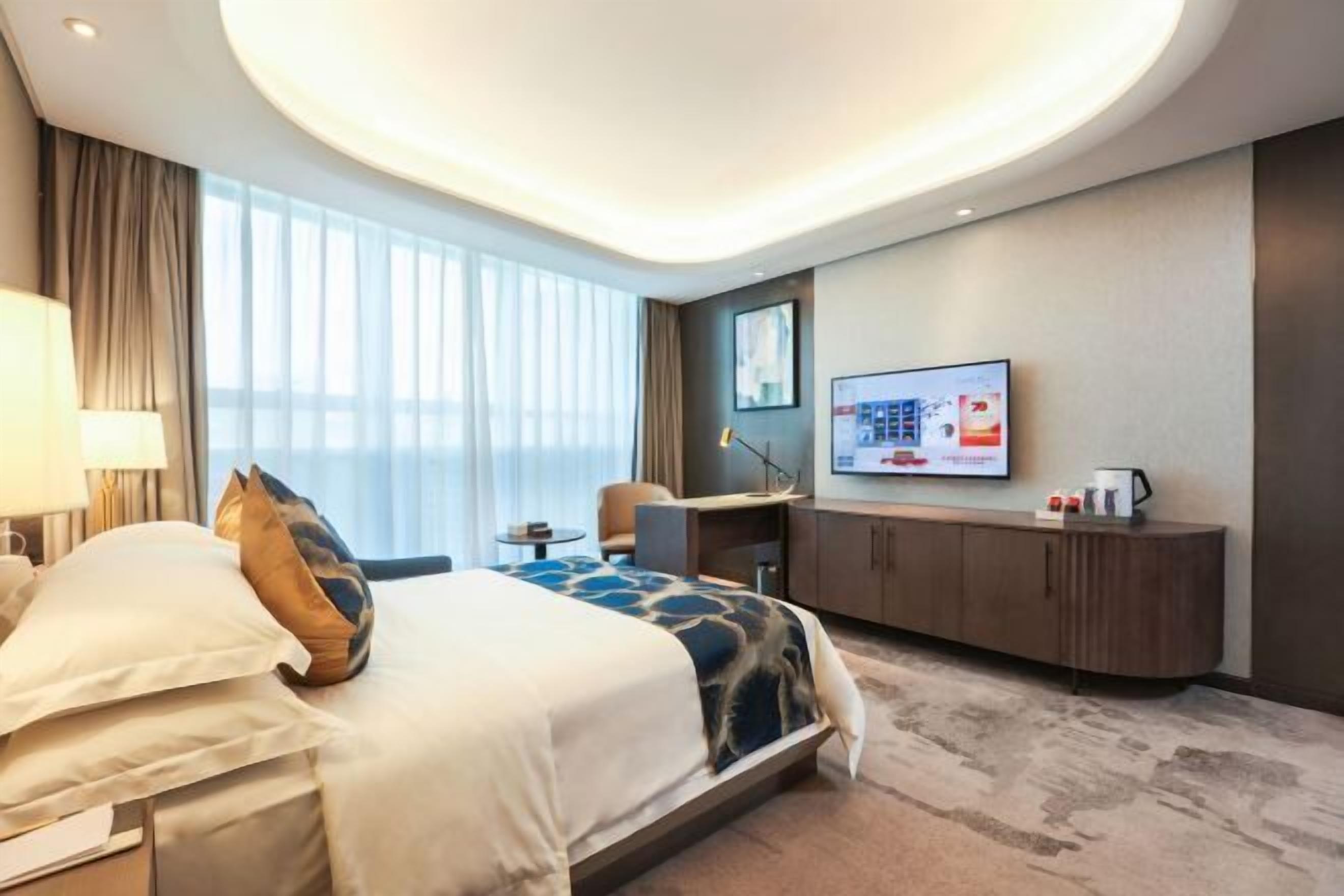 Ein modernes Hotelzimmer mit einem großen Bett, einem Schreibtisch, einem Fernseher und Blick auf die Stadt.