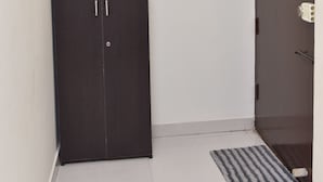 Una habitación con un armario de madera oscura, una puerta blanca con mirilla y una pequeña alfombra en el suelo.