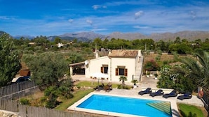 Uma villa com piscina, rodeada por vegetação e montanhas ao fundo.