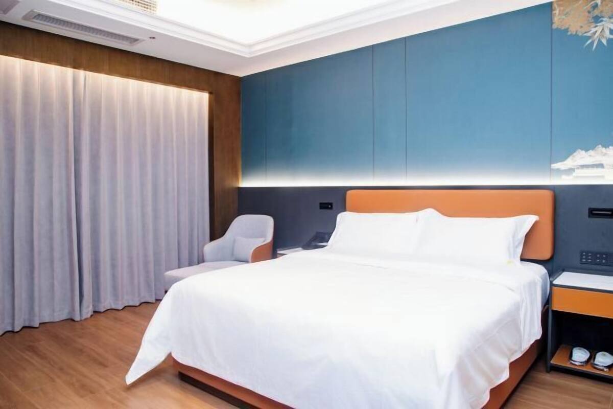 A hotel room with a large bed, a bedside table, a chair, and a curtain.