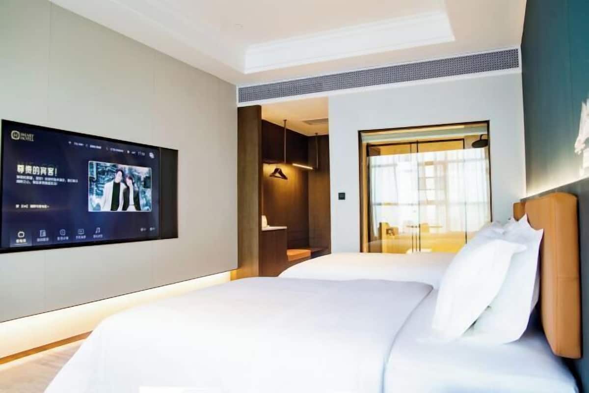 A hotel room with a bed, a TV mounted on the wall, and a view of the outside.