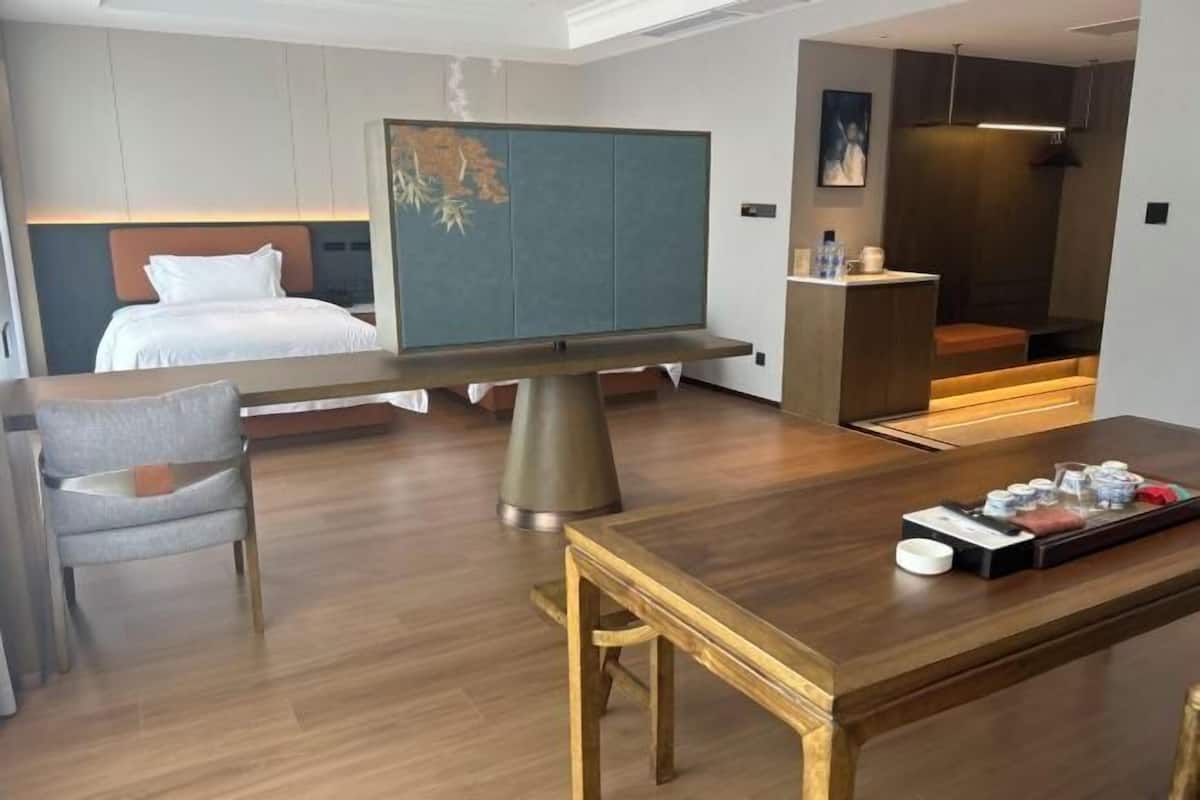 A hotel room with a bed, a desk, a chair, a table, a sofa, and a small kitchen area.