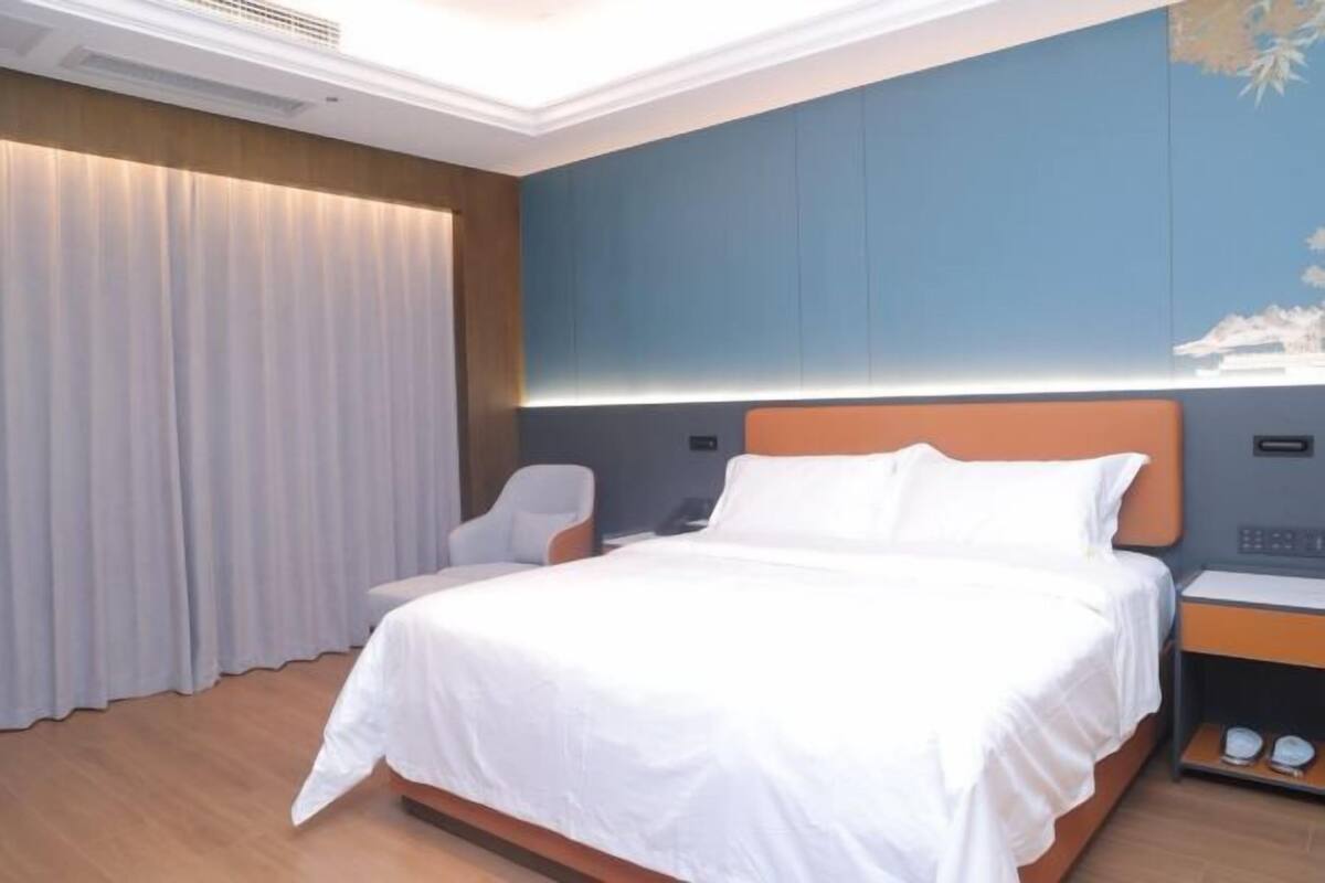 A hotel room with a bed, a chair, a nightstand, and a curtain.