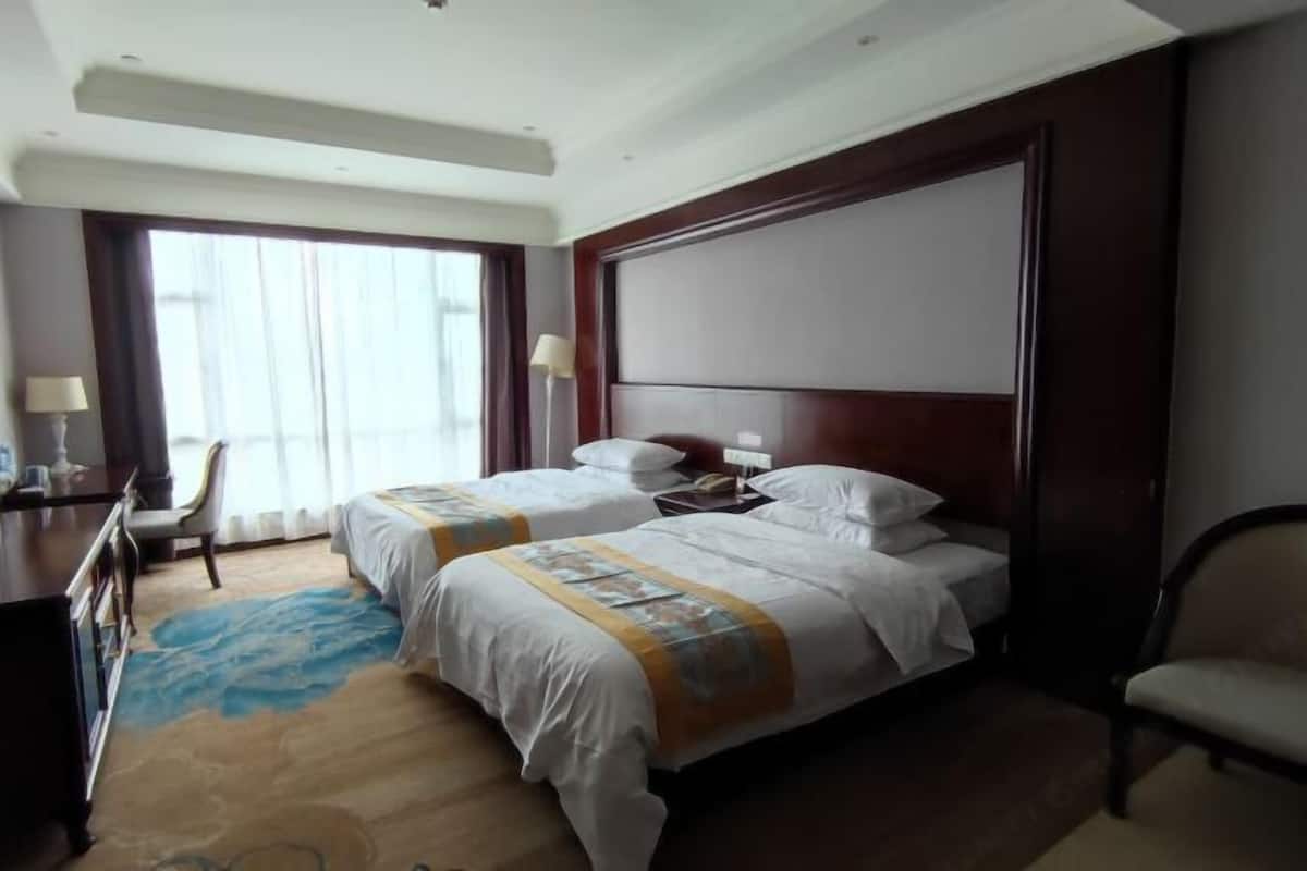 A hotel room with two beds, a desk, a chair, and a large window.
