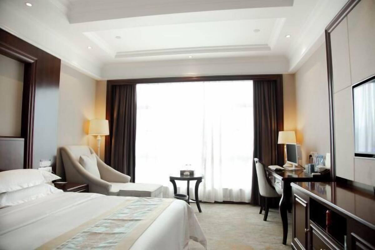 A hotel room with a bed, a desk, a chair, a TV, and a window with curtains.