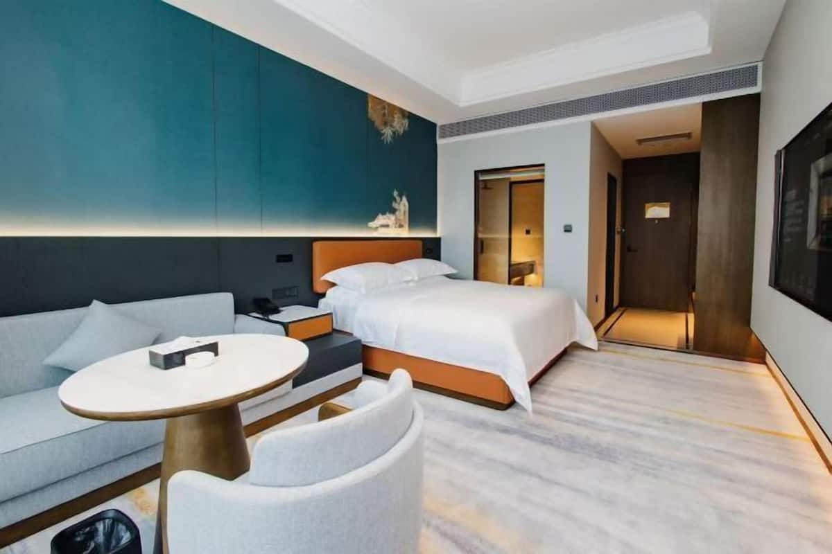 A modern hotel room with a bed, sofa, and a small table.