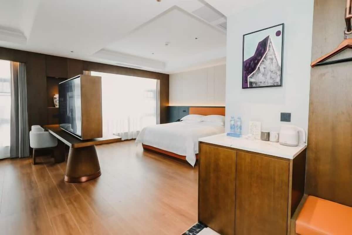 A modern hotel room with a bed, a desk, a chair, a TV, and a painting on the wall.