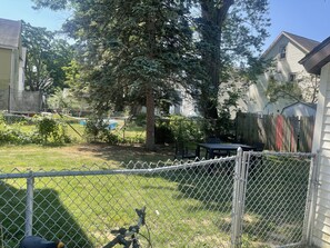 A fenced backyard with a table and chairs, a large tree, and a house in the background. - Kid friendly neighborhood!  Everyone is welcomed in this cozy apartment home! (Springfield)