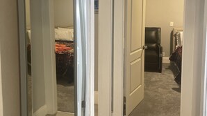 A hallway with a mirrored closet door, a bed with a patterned blanket, and a black chair. - Kid friendly neighborhood!  Everyone is welcomed in this cozy apartment home! (Springfield)