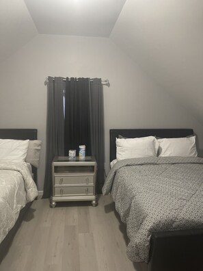 A bedroom with two beds, a nightstand with a can and a small item, and a window with dark curtains. - Kid friendly neighborhood!  Everyone is welcomed in this cozy apartment home! (Springfield)