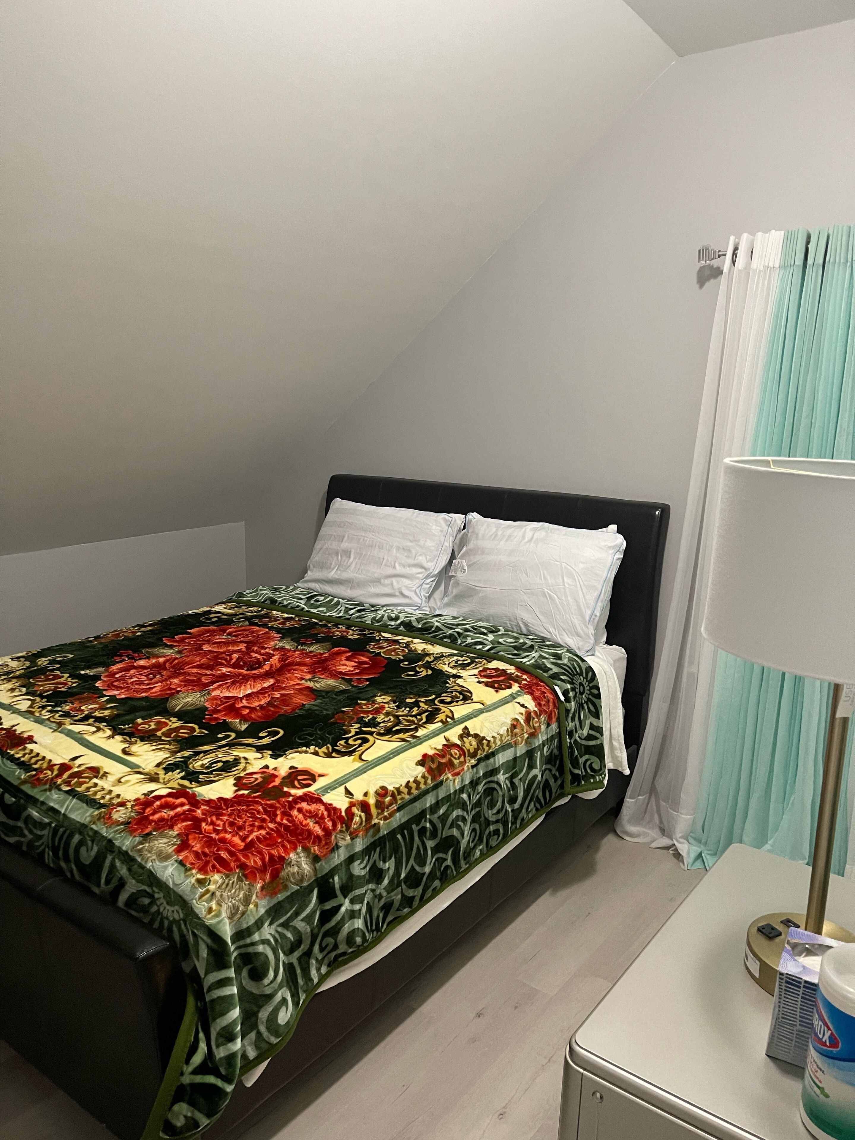 Une chambre à coucher avec un lit, une table de chevet, une lampe et une fenêtre avec des rideaux.