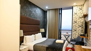 Habitació d'hotel amb un llit gran, un escriptori, una cadira, una taula petita i vista a l'oceà.