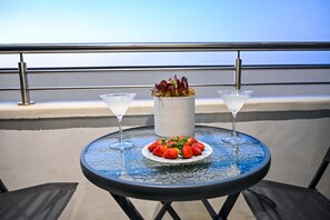 Una mesa redonda con cubierta de vidrio, dos vasos de martini, un plato de fresas y una planta en maceta en un balcón con barandilla.