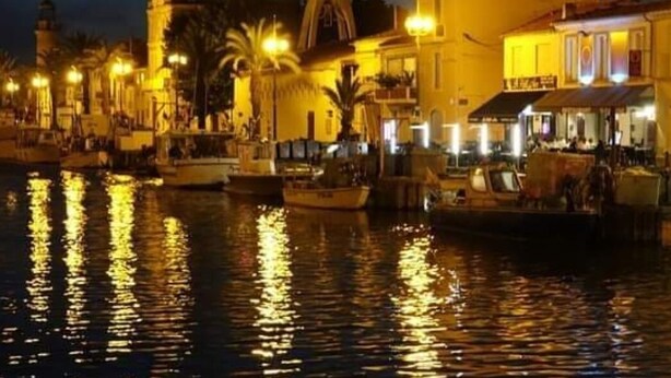 A waterfront area with boats docked, buildings with balconies, and street lamps along the water. - Mobile home in camping Le mas de l'isle (LUNEL)