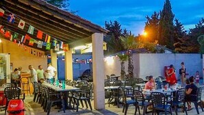 An outdoor dining area with tables and chairs, flags hanging above, and a building with a tiled roof in the background. - Mobile home in camping Le mas de l'isle (LUNEL)