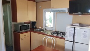 A compact kitchen with a microwave, stove, sink, and refrigerator. - Mobile home in camping Le mas de l'isle (LUNEL)