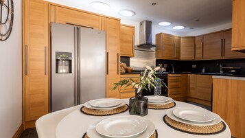 Una cocina moderna con armarios de madera, un refrigerador de acero inoxidable y una mesa de comedor con platos y un jarrón de flores.