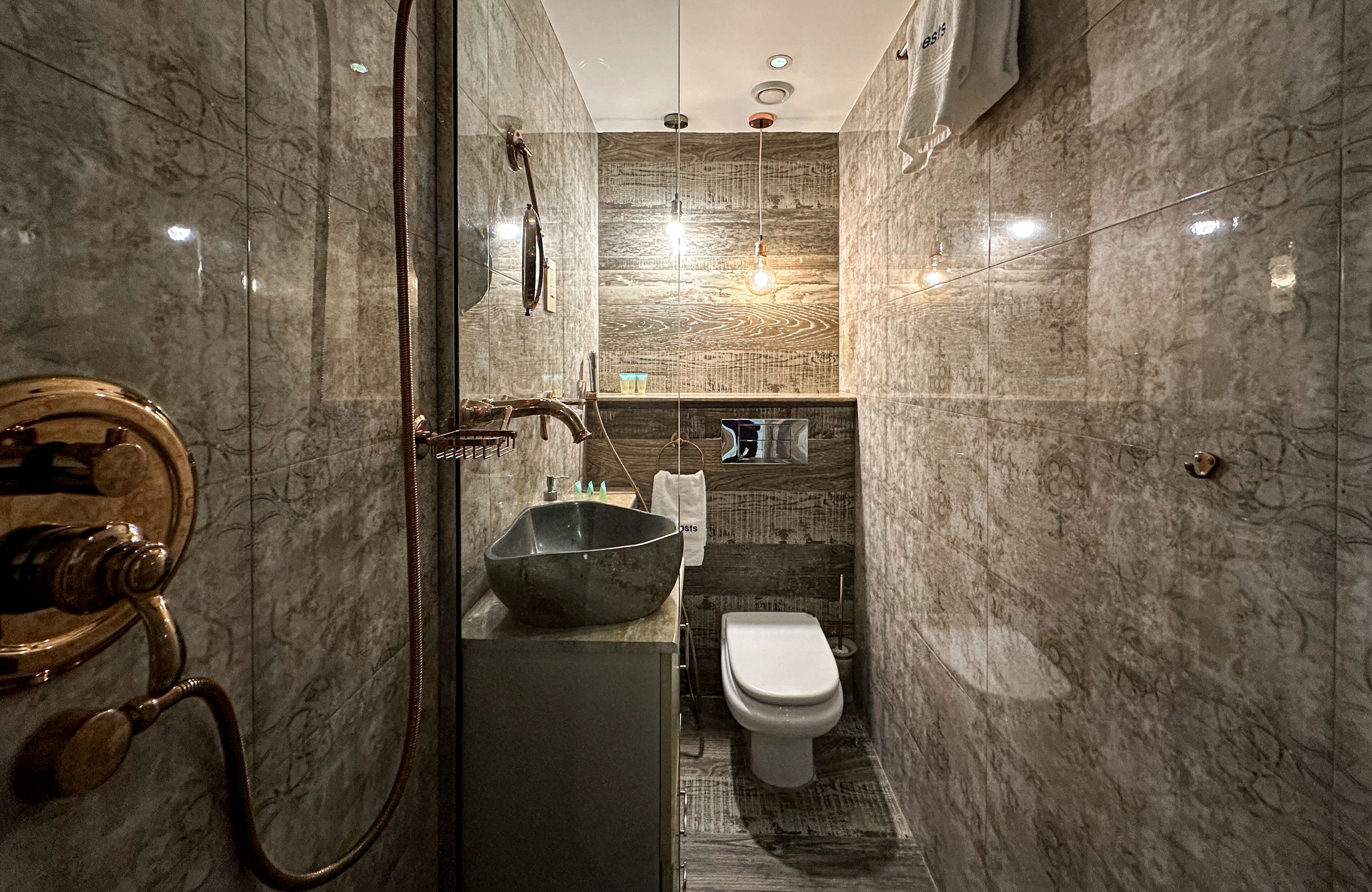 Une salle de bain moderne avec un mur en marbre, un grand lavabo, des toilettes et un espace douche.