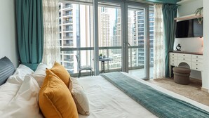 Une chambre d’hôtel avec un grand lit, un bureau avec une télévision et un balcon offrant une vue sur les grands immeubles.