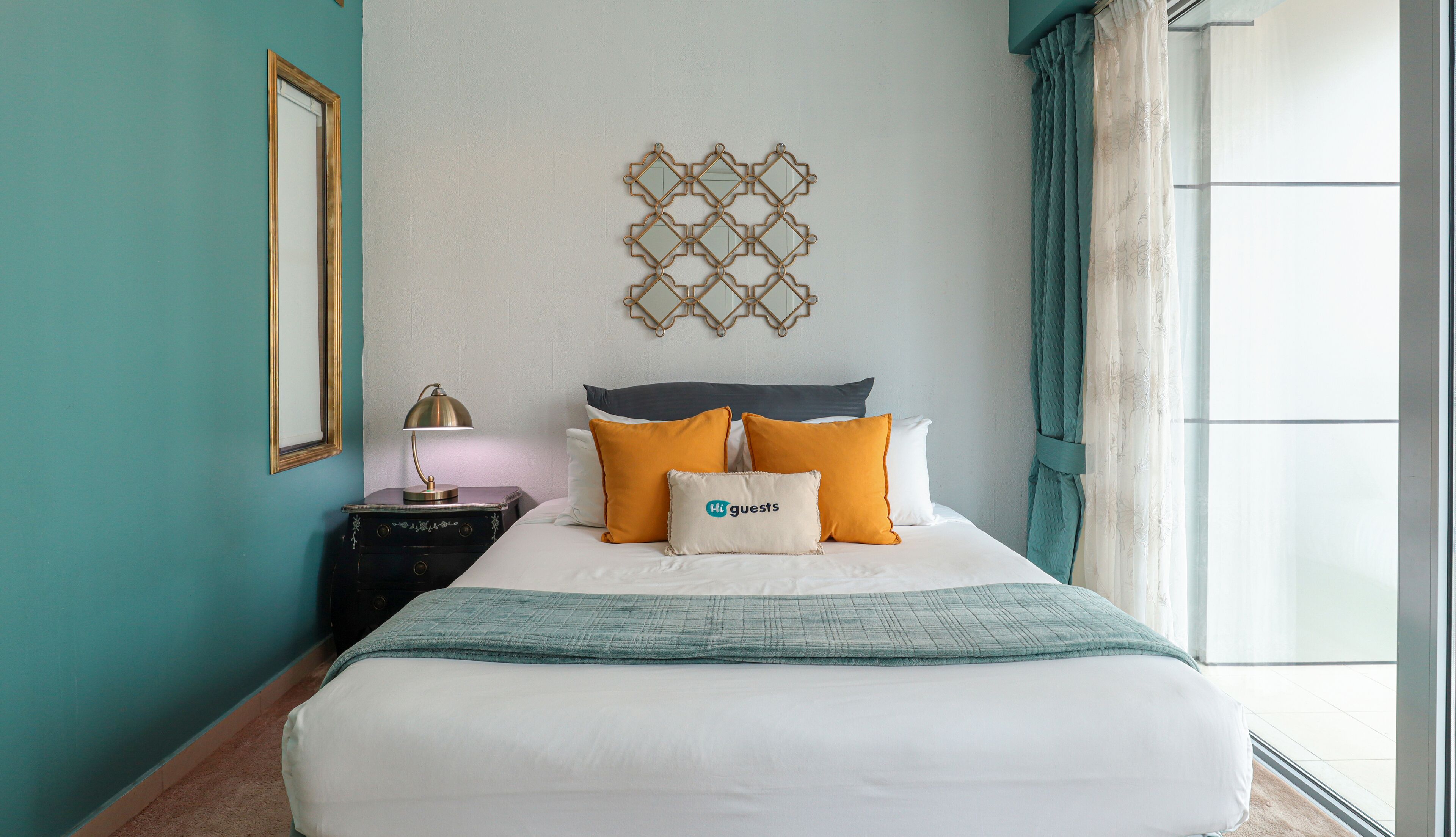 A neatly made bed with a teal blanket, a nightstand with a lamp, and a wall-mounted decorative piece.