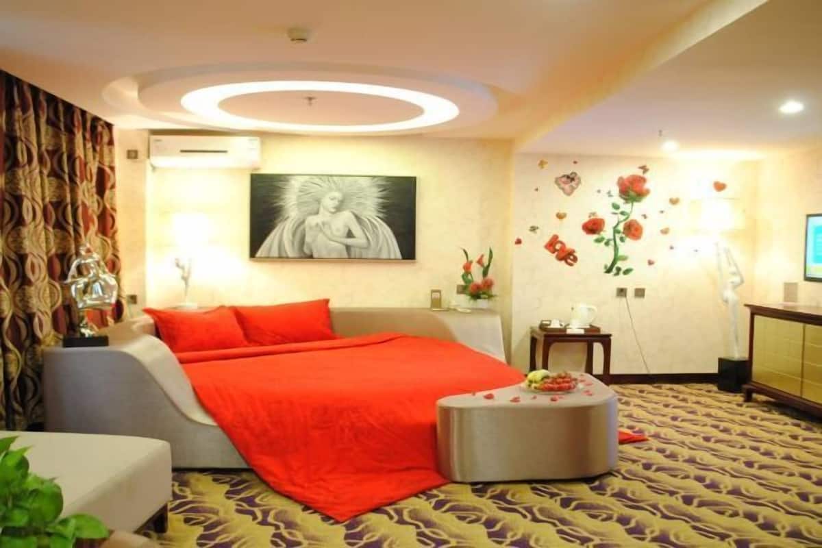 Ein Hotelzimmer mit Bett, rundem Tisch, Wand-Klimaanlage und einer Wand mit floralen und herzförmigen Verzierungen.