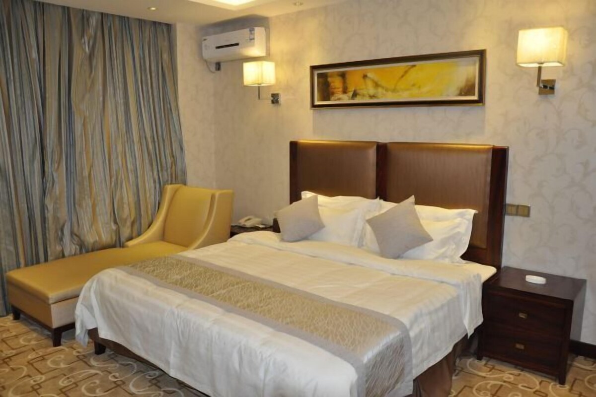 Habitación de hotel con cama, mesita de noche, una silla, aire acondicionado de pared y un cuadro.