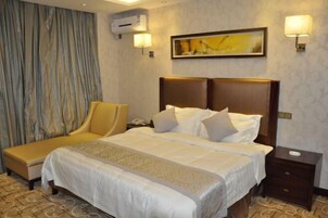 Habitación de hotel con cama, mesita de noche, una silla, aire acondicionado de pared y un cuadro.