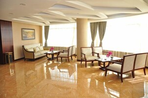 Un espacioso vestíbulo de hotel con piso pulido, un sofá, dos sillones, una mesita de centro y un amplio ventanal con cortinas.
