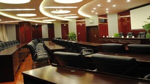 Un salón de conferencias con una larga mesa y sillas, luces empotradas en el techo y una pantalla de proyección.