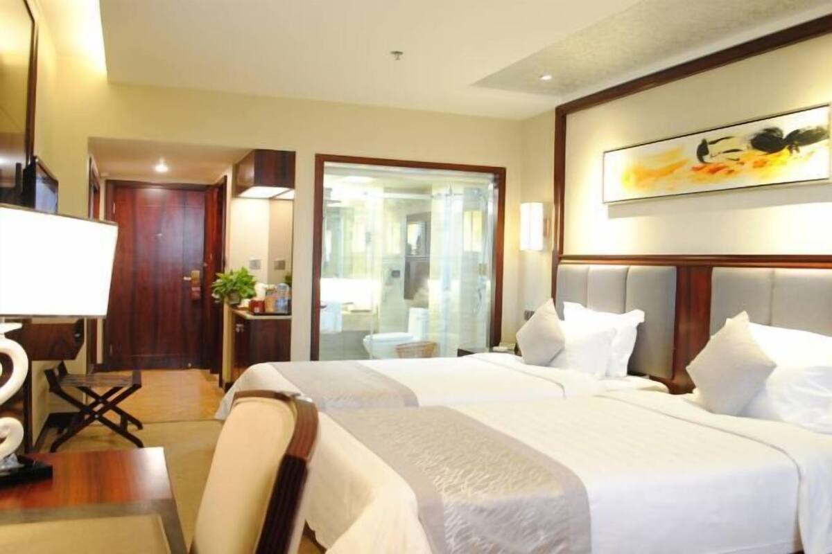 Ein Hotelzimmer mit zwei Betten, einem Schreibtisch, einem Stuhl, einem Spiegel und einem Bild an der Wand.
