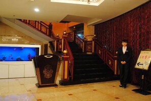 Un hall de hotel con una imponente escalera, una recepción y un muro decorativo.