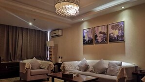 Un salón con sofá, sillones, una mesa de centro, una araña y cuadros en la pared.