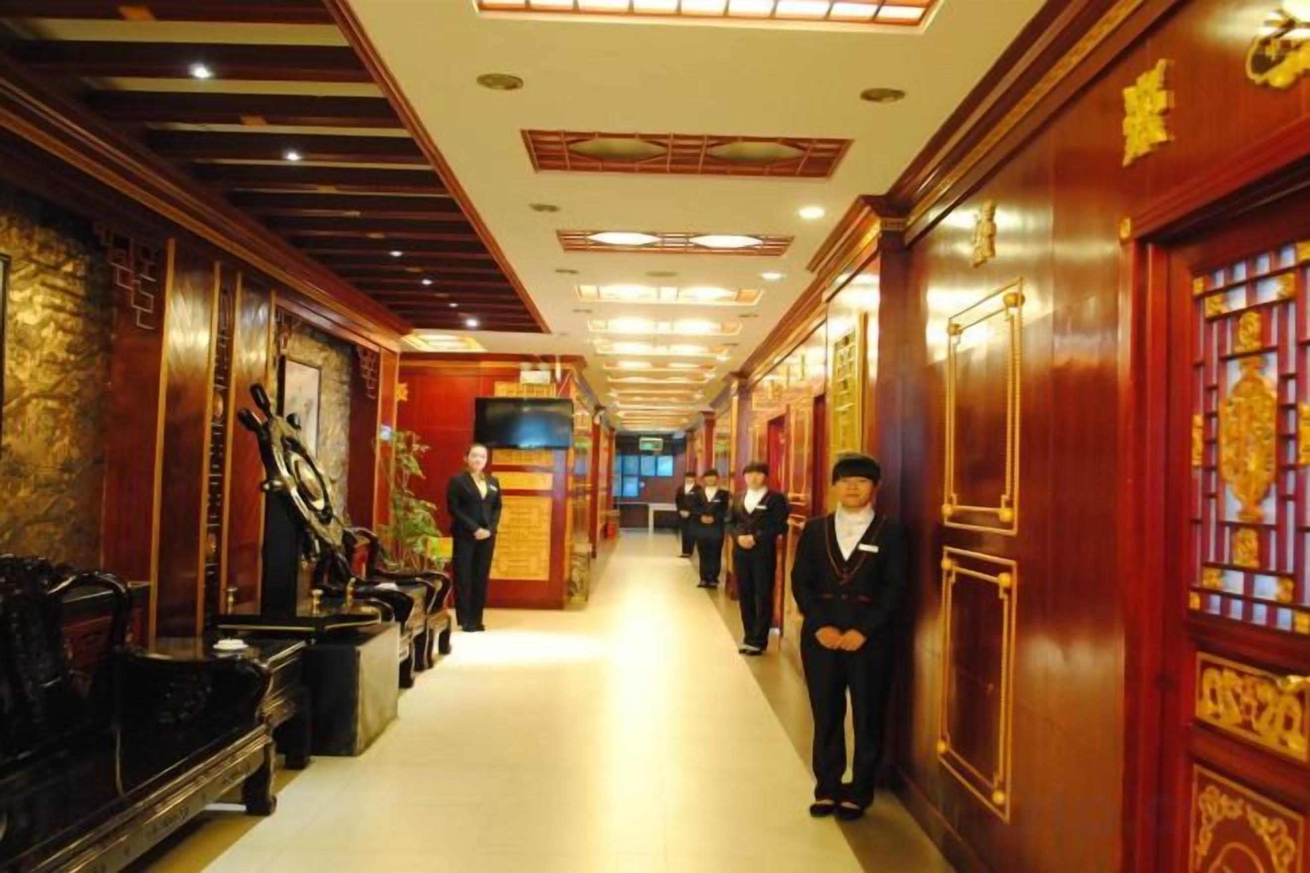 A hotel corridor with a long hallway, wooden paneling, and a reception area with staff.
