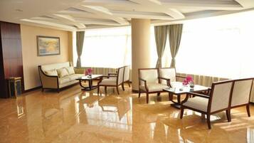 A spacious hotel lobby with a polished marble floor, a sofa, two armchairs, and a table with a vase of flowers.
