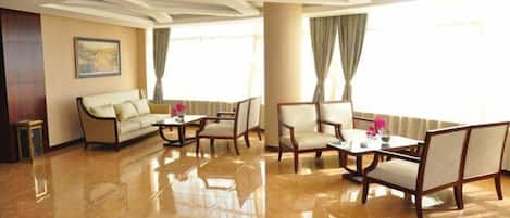 A spacious hotel lobby with a polished marble floor, a sofa, two armchairs, and a table with a vase of flowers.