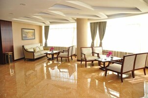 Un amplio vestíbulo de hotel con piso de mármol pulido, un sofá, dos sillones y una mesa con un jarrón de flores.