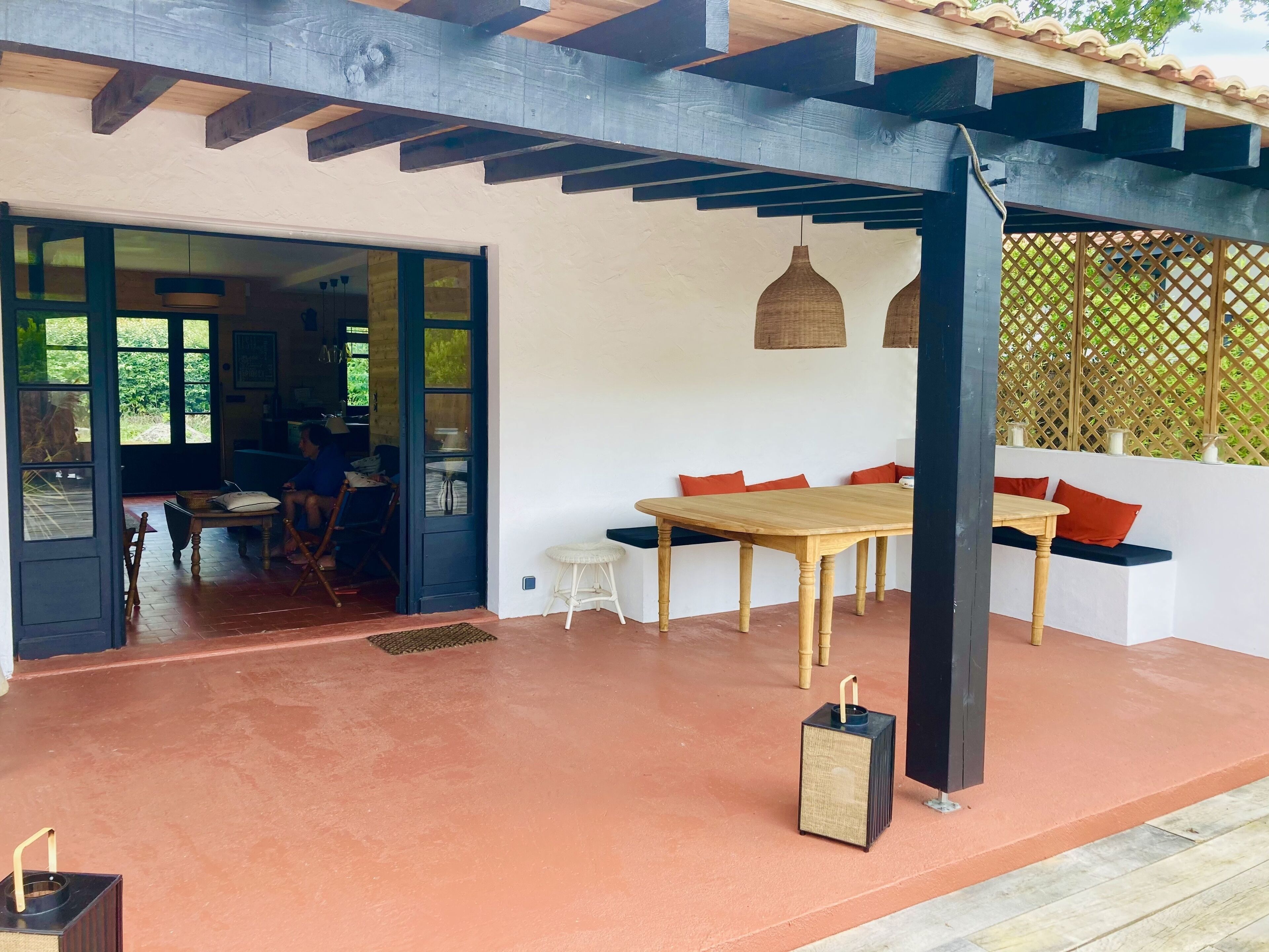 A covered patio area with a wooden table and benches, a small stool, and a speaker.