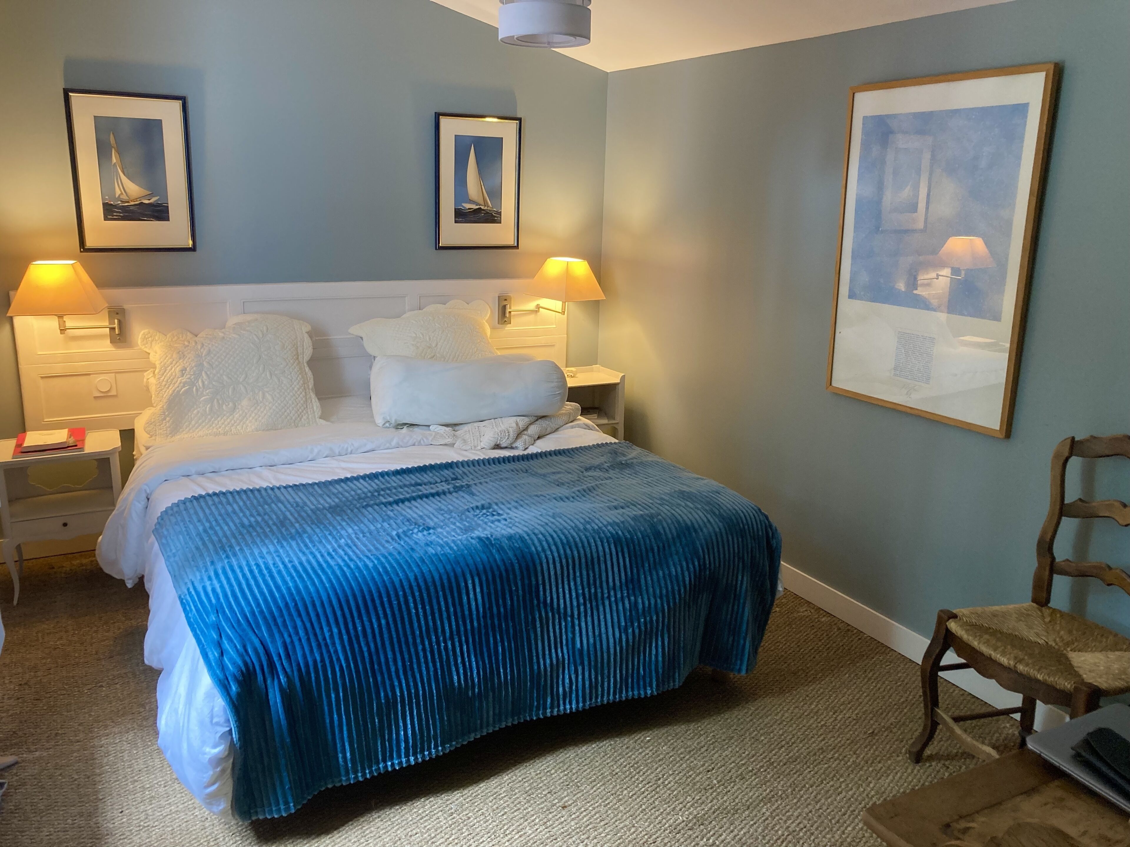 A bedroom with a bed, two bedside lamps, a chair, and three framed pictures on the wall.