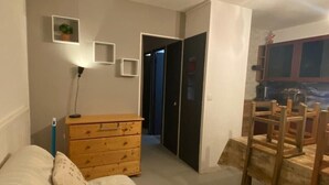 A bedroom with a bed, wooden dresser, and a desk with chairs. There are two doors, one leading to a closet and another to a hallway.