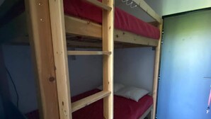 A bunk bed with a wooden ladder, a red mattress, and a white pillow.