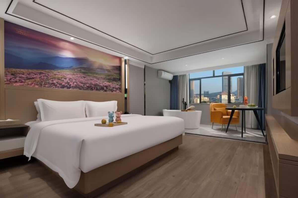 Una habitación de hotel moderna con una cama grande, un escritorio con silla y vistas de la ciudad a través de amplios ventanales.