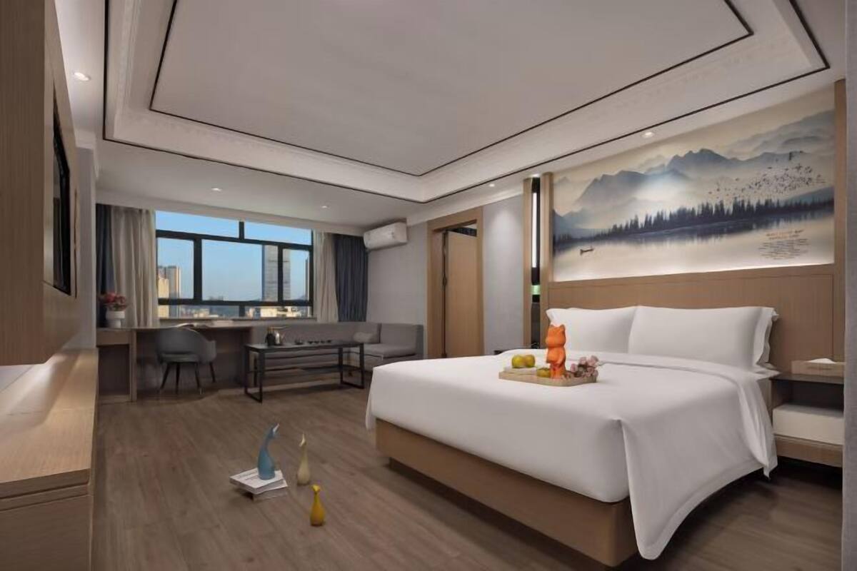 Habitación de hotel moderna con una cama grande, un escritorio y vistas de la ciudad a través de amplios ventanales.