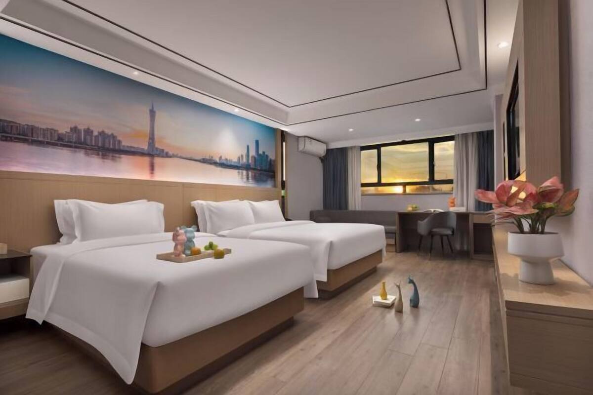 Habitación de hotel moderna con dos camas, un escritorio y un mural grande con vistas a la ciudad.