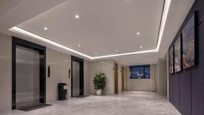 Un hall d'hôtel moderne avec un plafond haut, un éclairage encastré, une plante en pot et une vue sur la ville à travers les fenêtres.