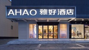 L’entrée d’un hôtel, avec une enseigne indiquant « AHAO 雅好酒店 » et une façade en verre laissant entrevoir la décoration intérieure.